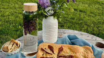 Focaccia bread, flowers, and water on a table outdoors.