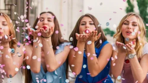 Women blowing confetti joyfully outdoors.