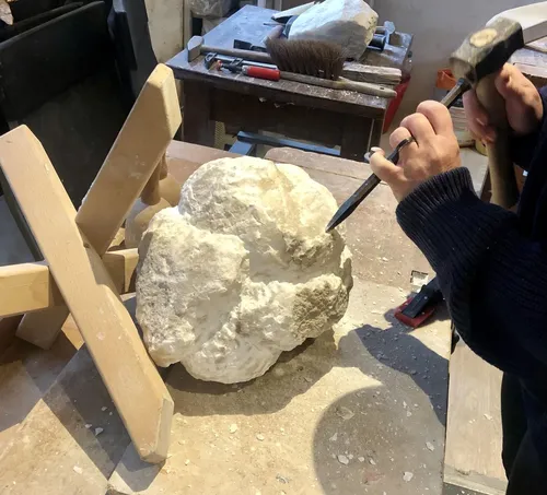 Sculptor carving stone with chisel in workshop.