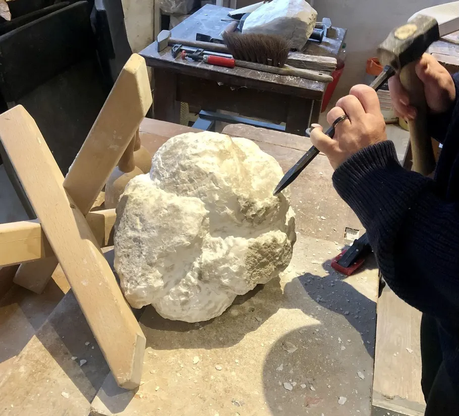 Sculptor carving stone with chisel in workshop.