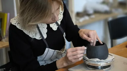 Frau modelliert Tonvase auf einem Tisch.