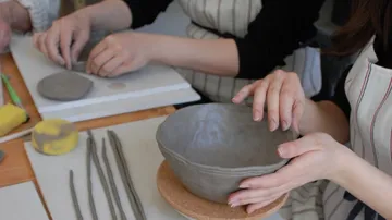 Hands crafting clay bowl on table