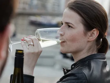 Woman drinks sparkling wine from a glass in an urban setting.