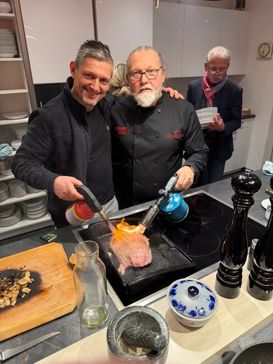 Two chefs torch beef in modern kitchen.