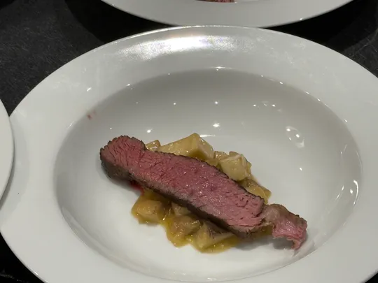 Steak slice on pasta in white bowl.