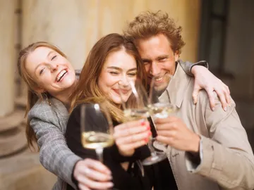 Three people toast with glasses, smile happily.