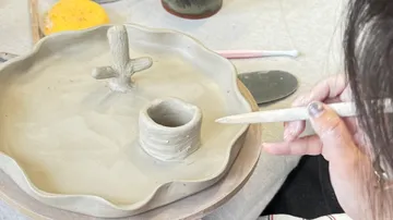 Person formt Tonskulptur auf Tisch.
