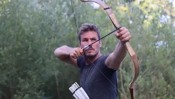 Archer aiming bow in wooded area