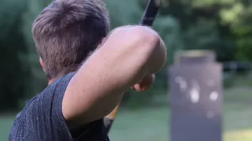 Person aiming archery bow outdoors.