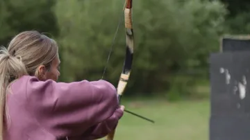 Person practicing archery outdoors in green field.