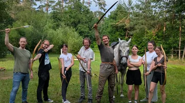 People posing with bows and swords outdoors.