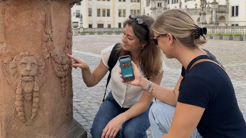 Zwei Personen betrachten eine Steinskulptur im Freien.