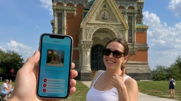 Person hält Handy, Frau lächelt, Kirche im Hintergrund.