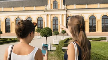 Zwei Frauen mit Handy besichtigen Gebäude draußen.