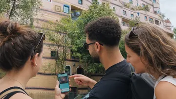 Drei Personen schauen auf Handy vor Gebäude.