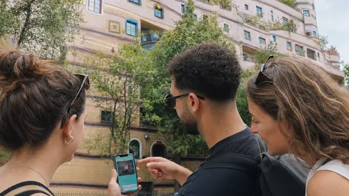 Three people examine phone outside colorful building.