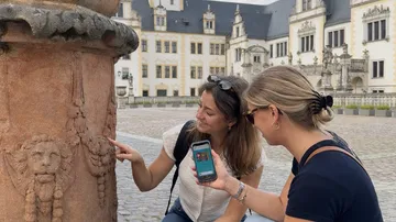 Zwei Frauen betrachten Skulptur vor historischem Gebäude.