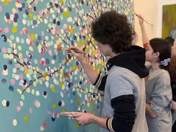 Menschen malen gemeinsam auf einer bunten Wand mit Ästen.