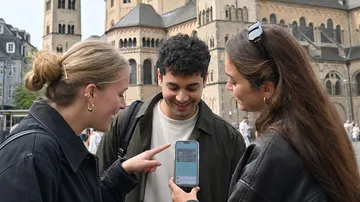 Three people view mobile phone outside cathedral.