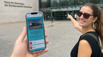 Woman pointing at museum, phone displaying quiz.