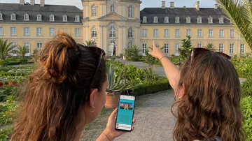 Two women view a yellow historic building.