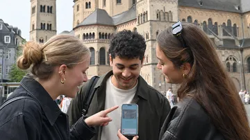 Three people looking at phone outside cathedral.