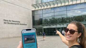 Frau zeigt lächelnd auf Museumseingang.