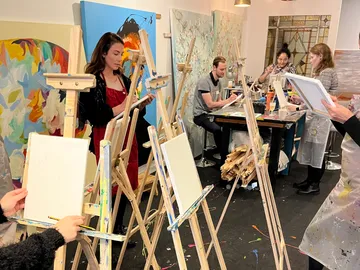 Personen malen an Staffeleien in einem kreativen Atelier.