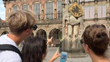 Drei Personen zeigen auf historische Statue.