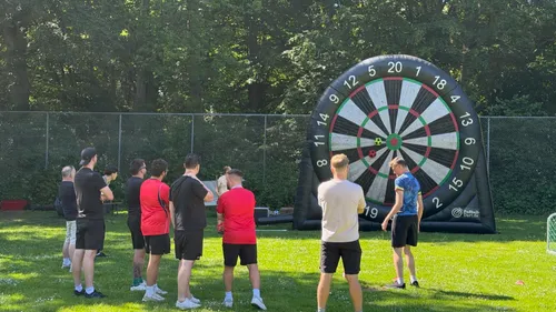 Gruppe spielt Darts auf aufblasbarer Scheibe draußen.