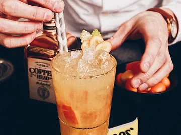 Ein Cocktail wird dekoriert, umgeben von einer Flasche und Früchten.