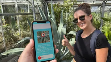Person hält Handy nahe Agavenpflanze.