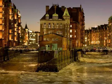 House on an island surrounded by water and illuminated buildings.