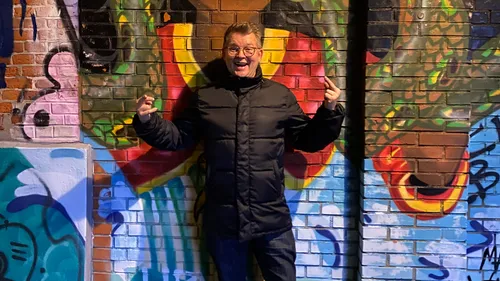 Mann posiert vor Graffiti-Wand.