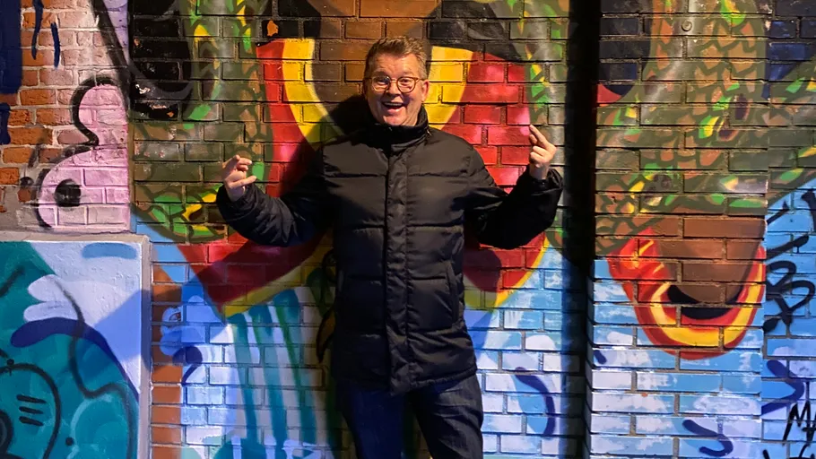 Man posing in front of graffiti wall.