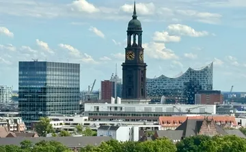 Clock tower overlooked by modern buildings, cloudy sky.