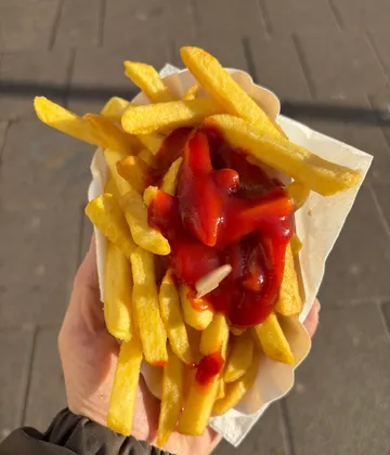Pommes mit Ketchup in Hand draußen.