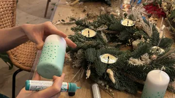 Person dekoriert Kerze neben Festtagskranz.
