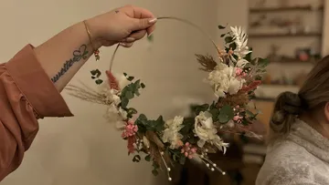 Hand hält Blumenkranz drinnen.