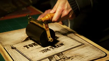 Hand walzt Tinte auf Holzschnittdruck.