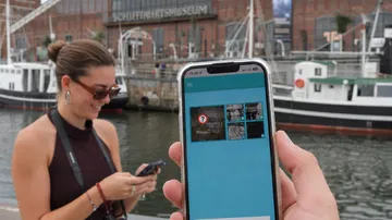 Person mit Handy bei historischen Schiffen.