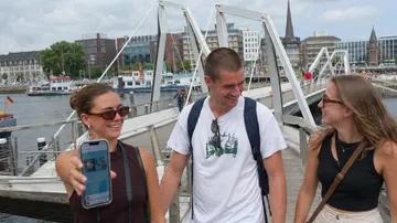 Drei Freunde spazieren auf einer Flussbrücke.