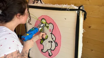 Frau benutzt Tufting-Pistole auf Leinwand