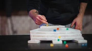 Hand placing dice on tiered platform.