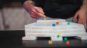 Hand stacking dice on layered platform.