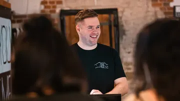 Man smiling, standing in a brick-walled room.