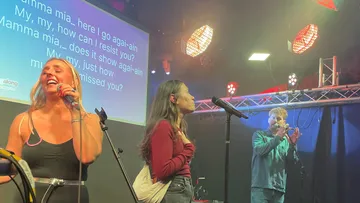 People singing karaoke on stage with lyrics.