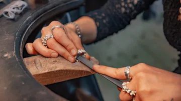 Hands filing jewelry on a wooden bench.