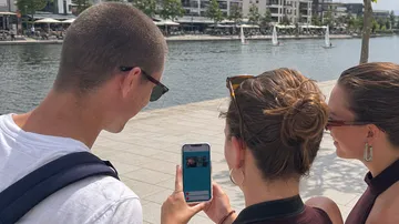 People looking at phone near waterfront.