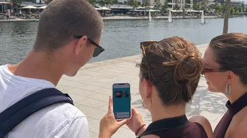 Drei Personen schauen auf Handy am Wasser.